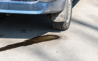 Drops of gasoline flow on asphalt from a parked car.