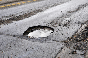 A large pothole in a road that has been damaged by rain, snow, and ice that is in need of repair.