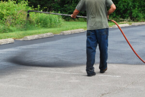 A man spraying a sealcoating material on an asphalt driveway