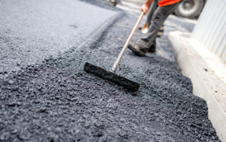 Worker levelling fresh asphalt on a road construction site, industrial buildings and teamwork